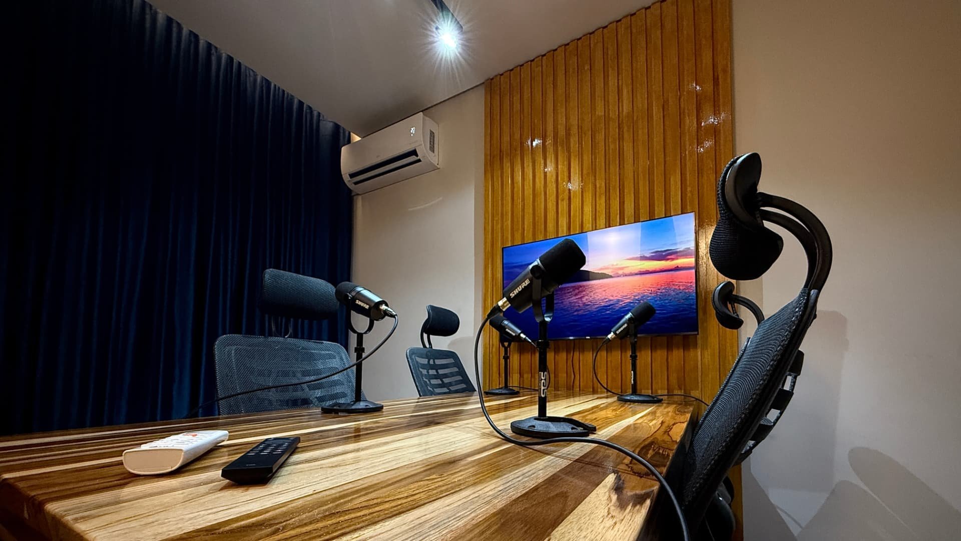 Mesa de gravação do Estúdios Japan Mídias com microfones, poltronas e tela